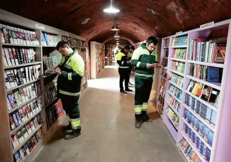People in reflective uniforms browsing books in a tunnel-like library.