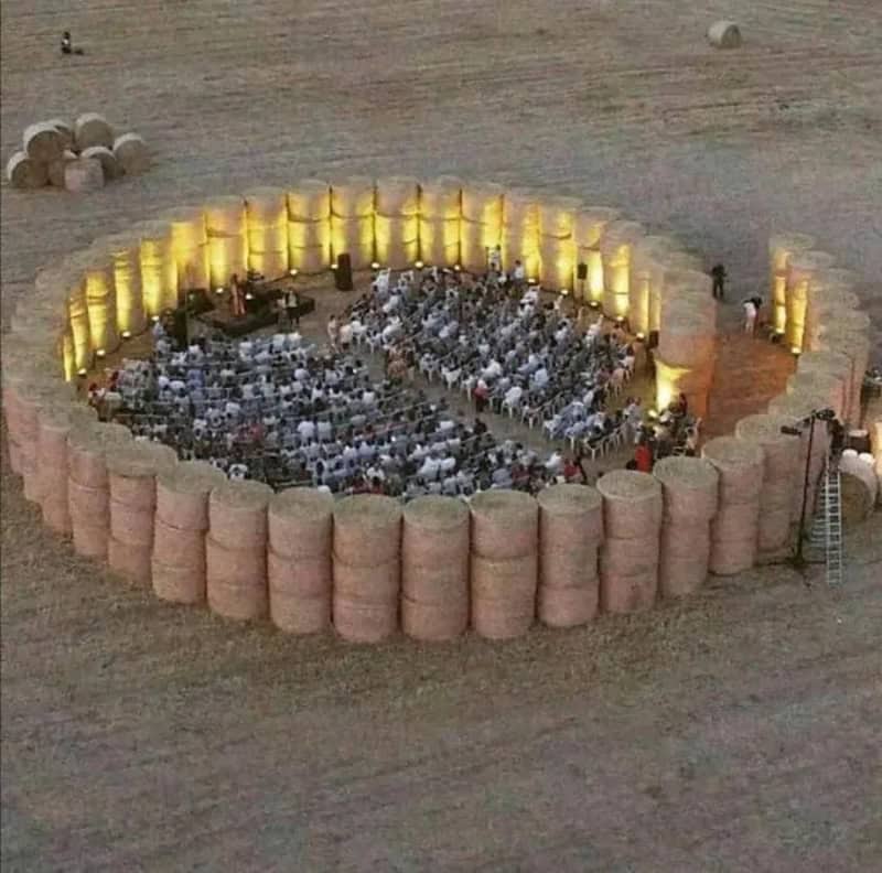 Large outdoor event inside a circular wall of hay bales at sunset.