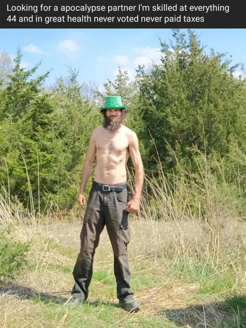 Man with a beard, green hat, shirtless, standing outdoors in a grassy field.