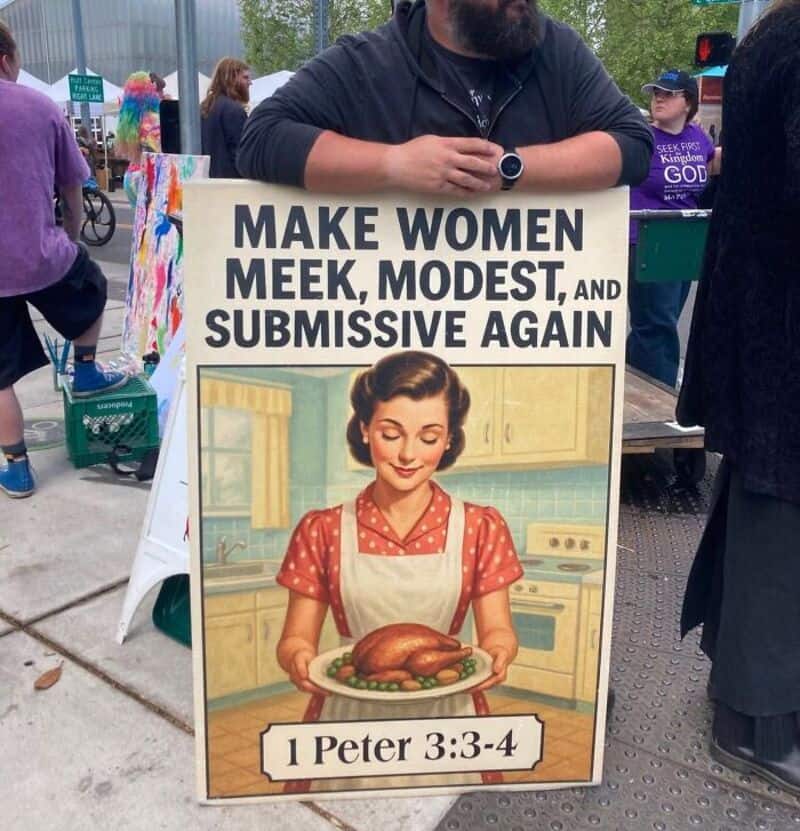 Protest sign reading 'Make women meek, modest, and submissive again' with a vintage illustration of.