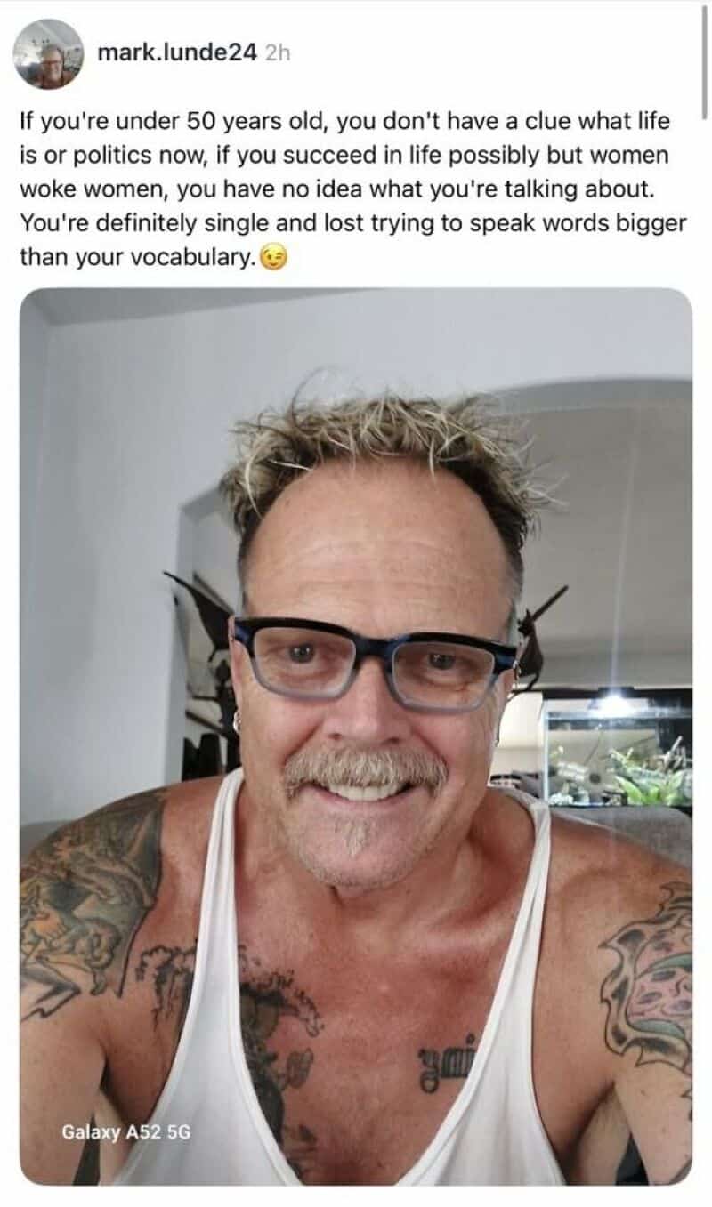 A man with glasses, tattoos, and a white tank top smiling at the camera.