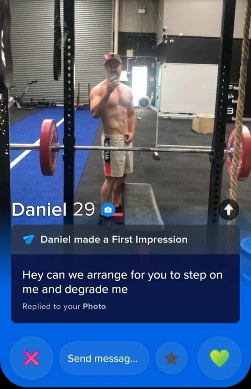 A shirtless man taking a mirror selfie in a gym, with weights and equipment in the background.