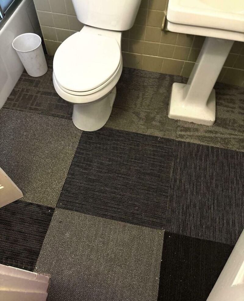 Bathroom with mismatched carpet tiles and a toilet.