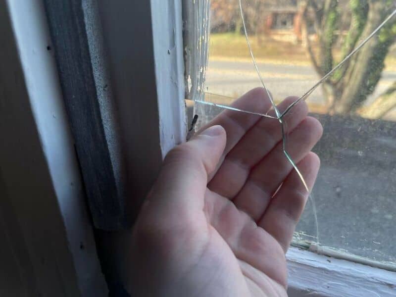 Hand holding a broken piece of glass in front of a window.