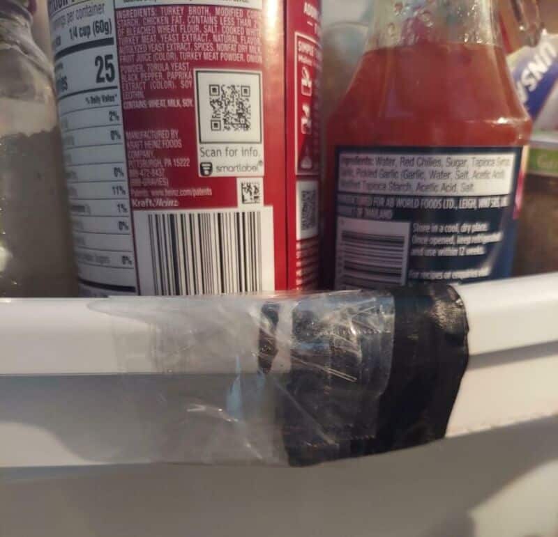 Close-up of a refrigerator shelf with a plastic wrap and two bottles, one with a barcode and QR code.