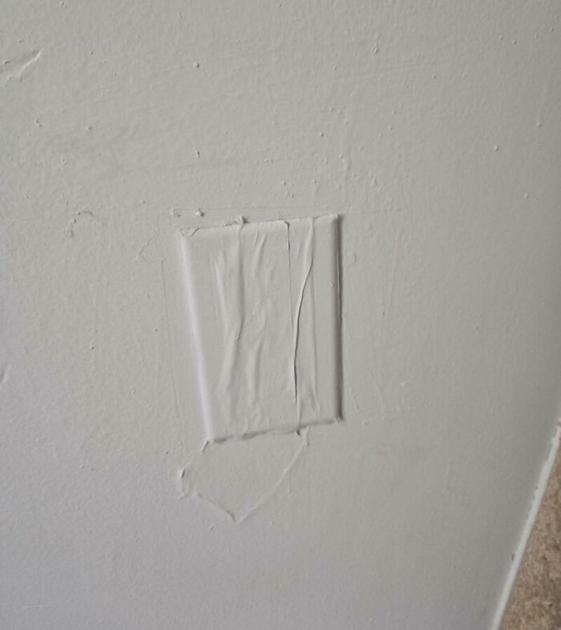A wall with a patch covering a damaged area, taped and painted over.