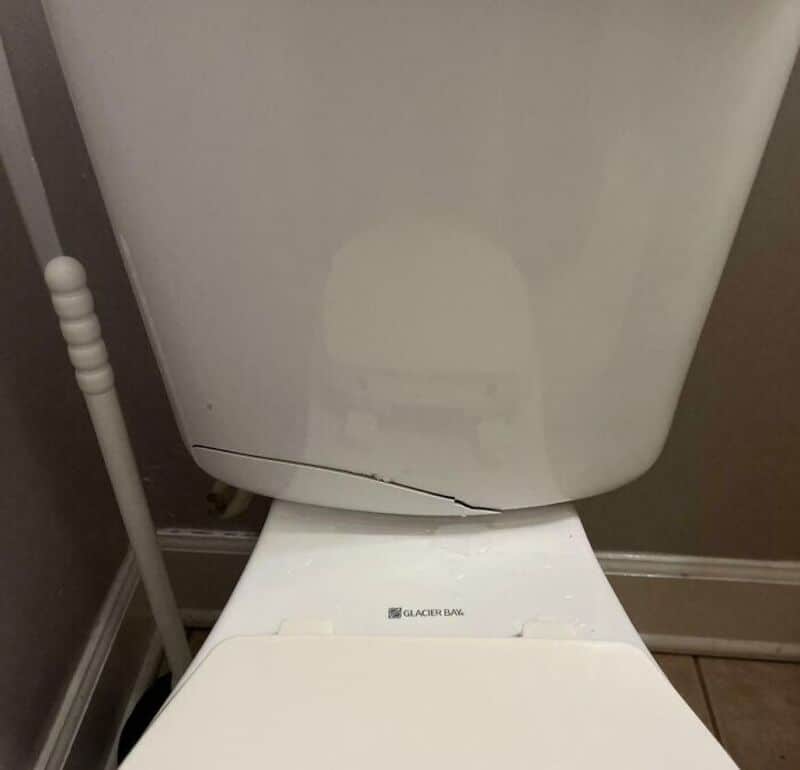 Cracked toilet tank with a visible crack at the bottom edge.