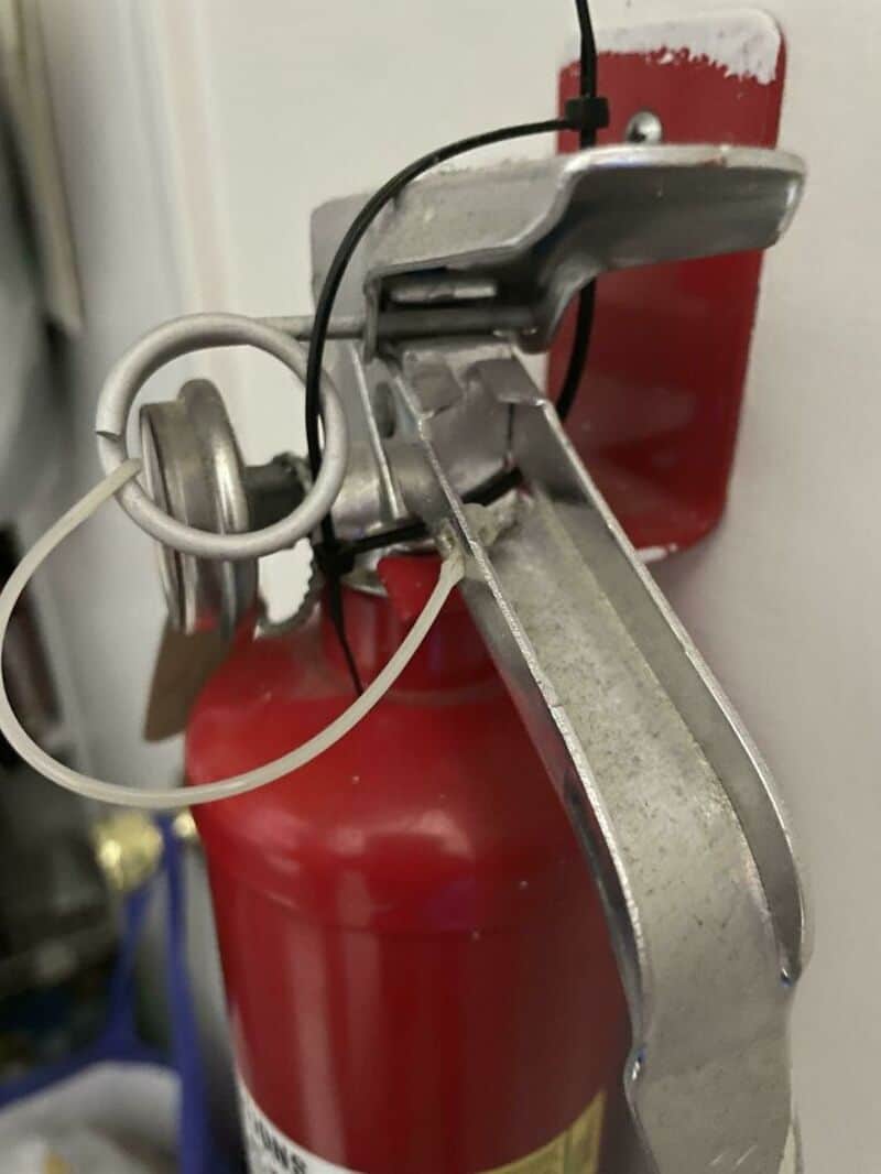 Fire extinguisher with a metal lever and safety pin, mounted on a wall.