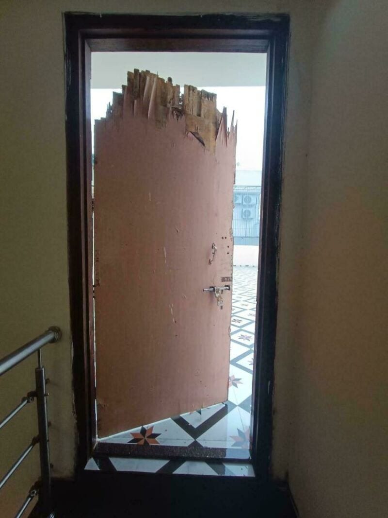 Damaged door with peeling wood and broken top, leading outside.
