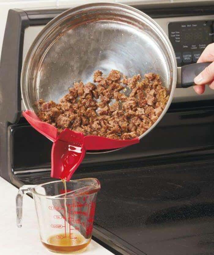 Pouring cooked ground beef from a pan into a measuring cup on a stove.