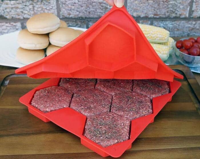Red silicone burger press with burger patties inside, on a wooden table.