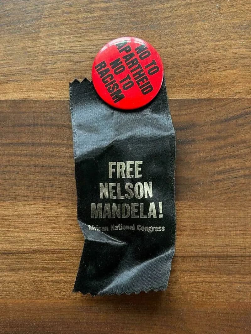 Button and ribbon with anti-apartheid messages, 'NO TO APARTHEID' and 'FREE NELSON MANDELA!'.