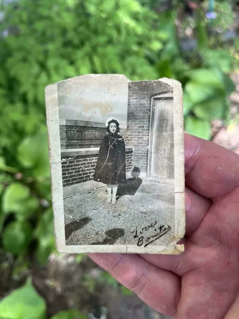 Black and white vintage photo of a girl standing outside near a brick wall.