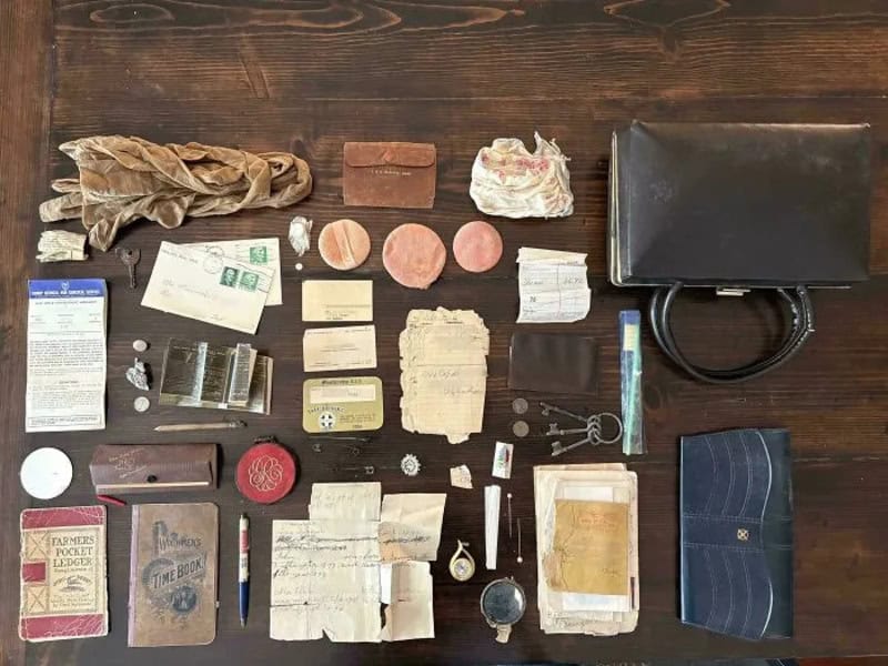 Collection of vintage papers, a black bag, and various small items on a wooden surface.