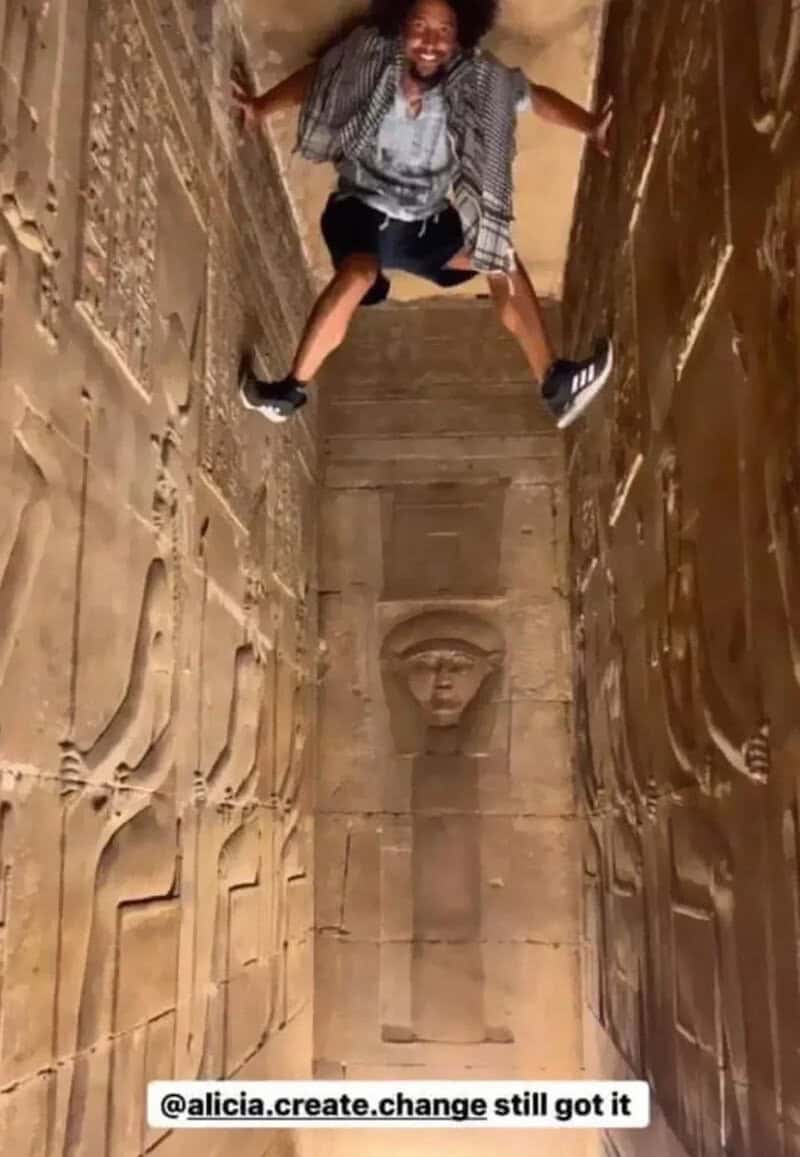Person hanging upside down in a narrow, ancient Egyptian tomb corridor.