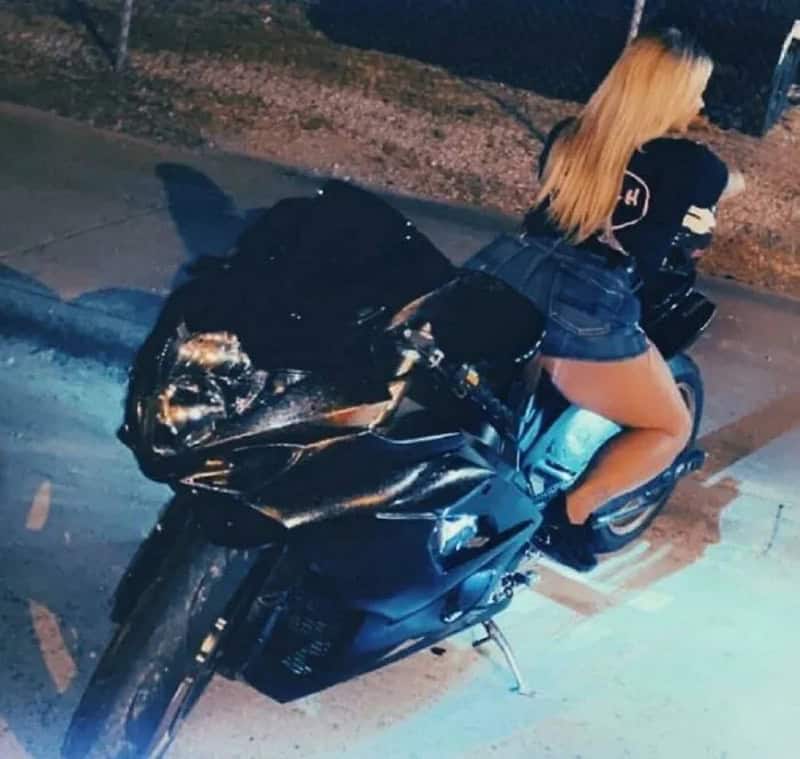 Blonde woman in denim shorts riding a black motorcycle at night.