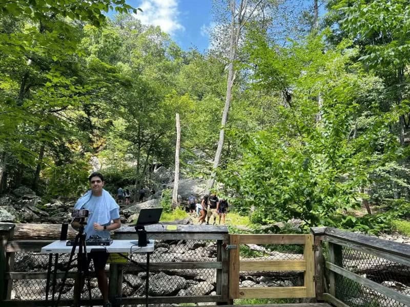Man DJing outdoors near a river in a forested area.