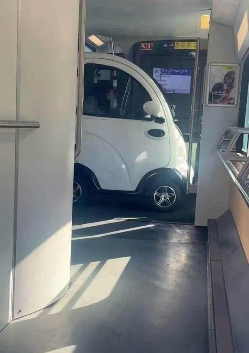 Small white car stuck in a train station doorway.