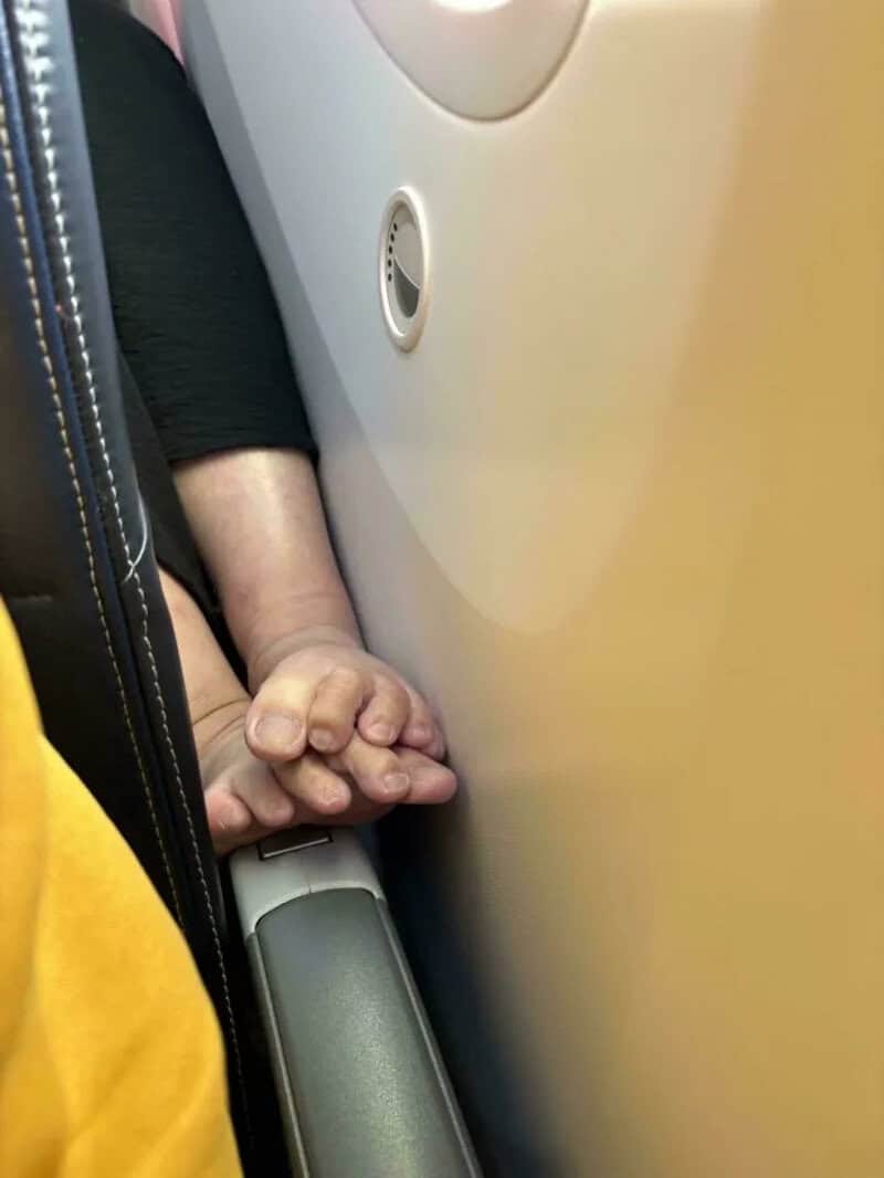 Child's hand holding an adult's finger on an airplane seat.
