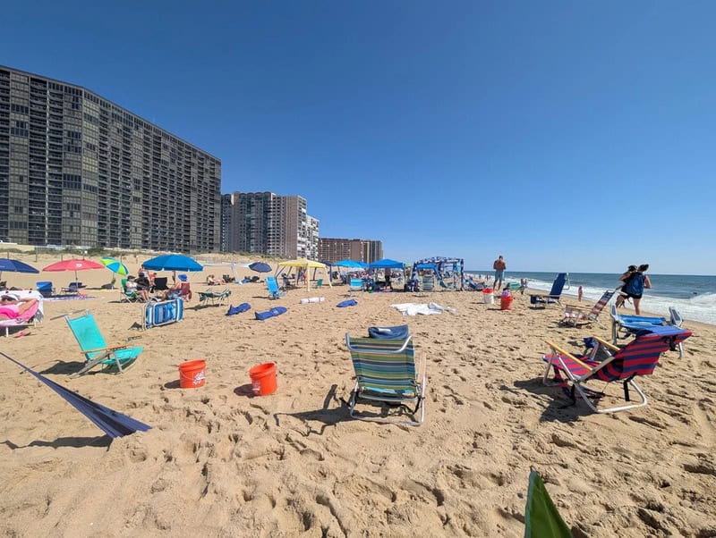 Beach scene with chairs, umbrellas, and buildings in the background.