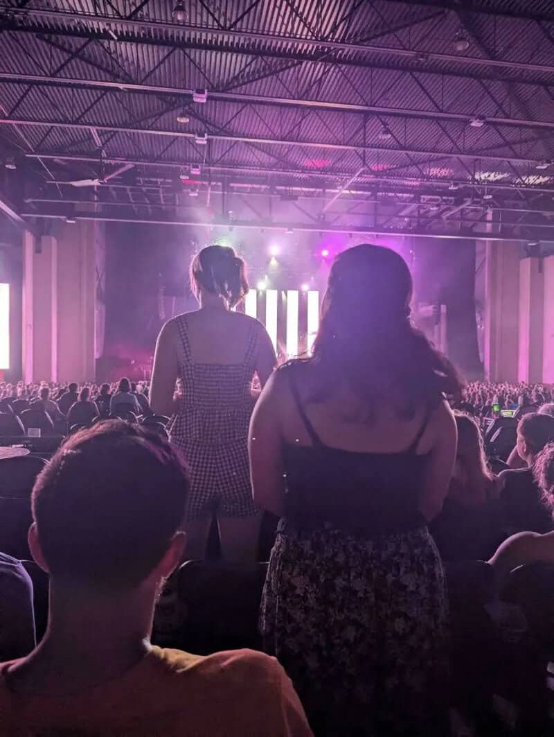 People watching a concert with purple and pink stage lights in a large indoor venue.