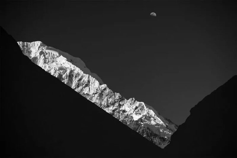 Snow-capped mountain peaks with the moon in the night sky.