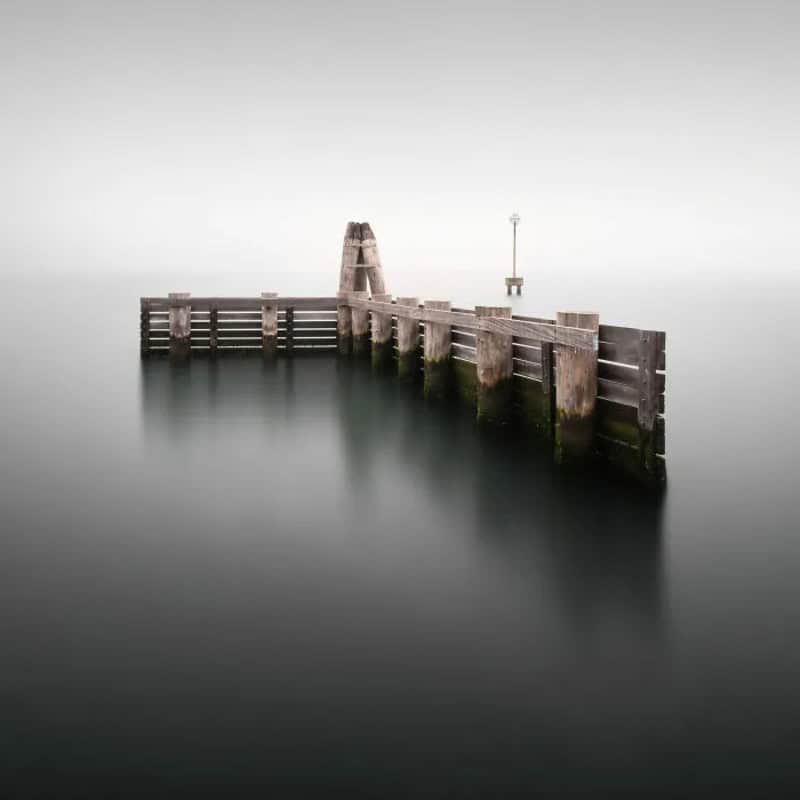 Minimalist pier extending into calm water with a small tower at the end.