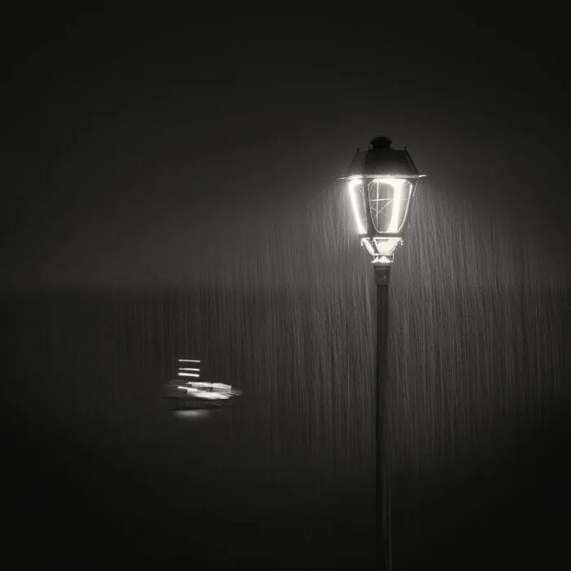 Streetlamp illuminating rain at night, with a blurred car in the background.