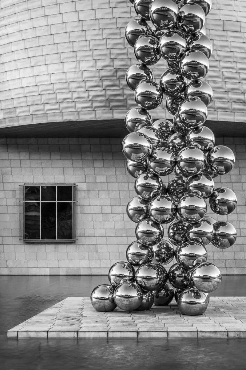 Sculpture of shiny metallic spheres stacked vertically in a modern gallery.