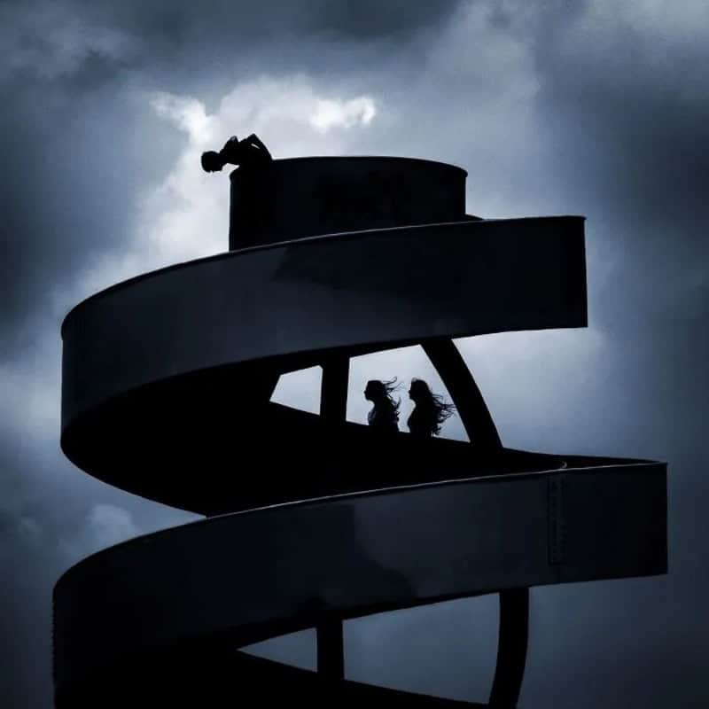Silhouette of two children on a spiral slide against a cloudy sky.