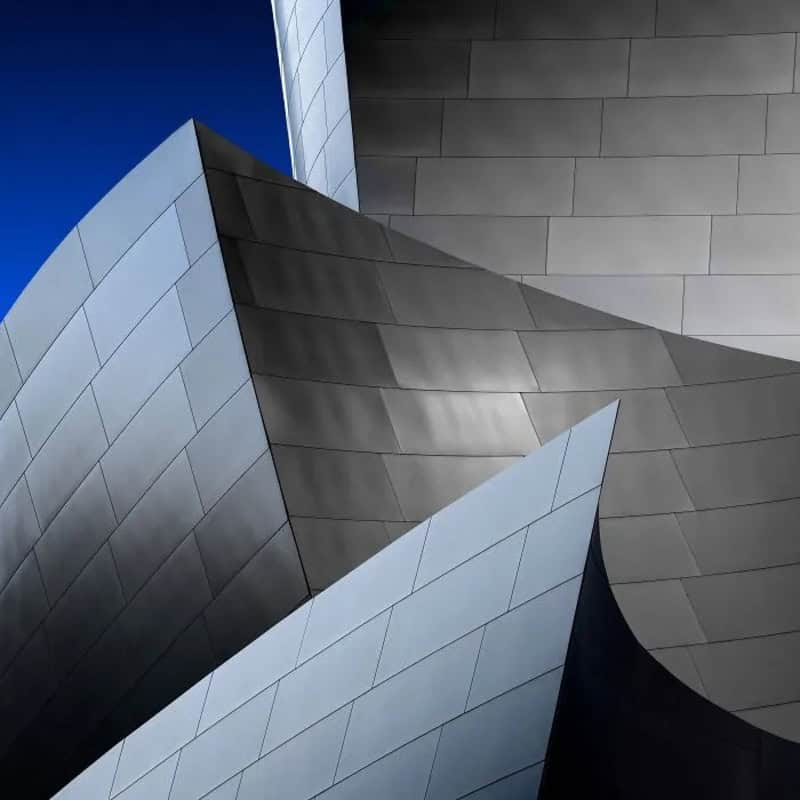 Modern building with geometric metallic surfaces and sharp angles under a blue sky.