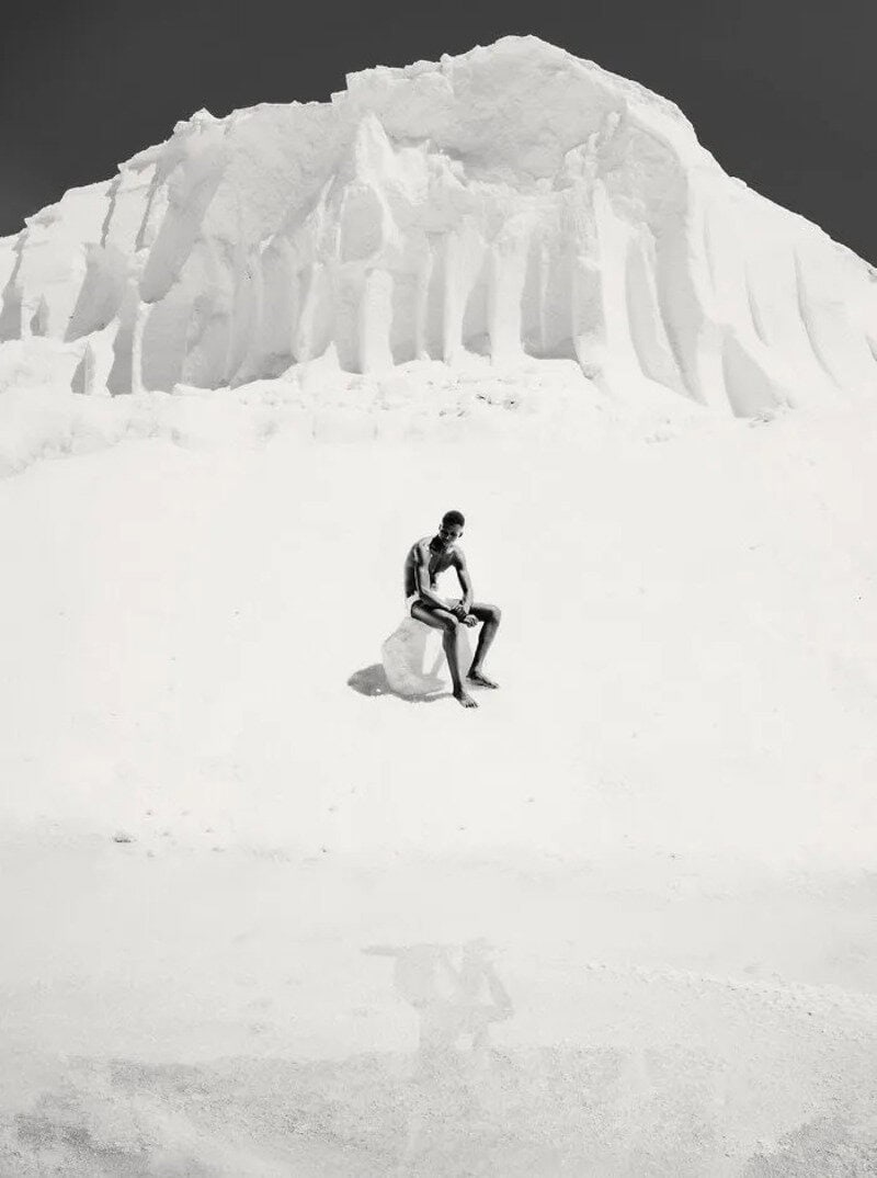 Person sitting on snow with large ice formation in background.
