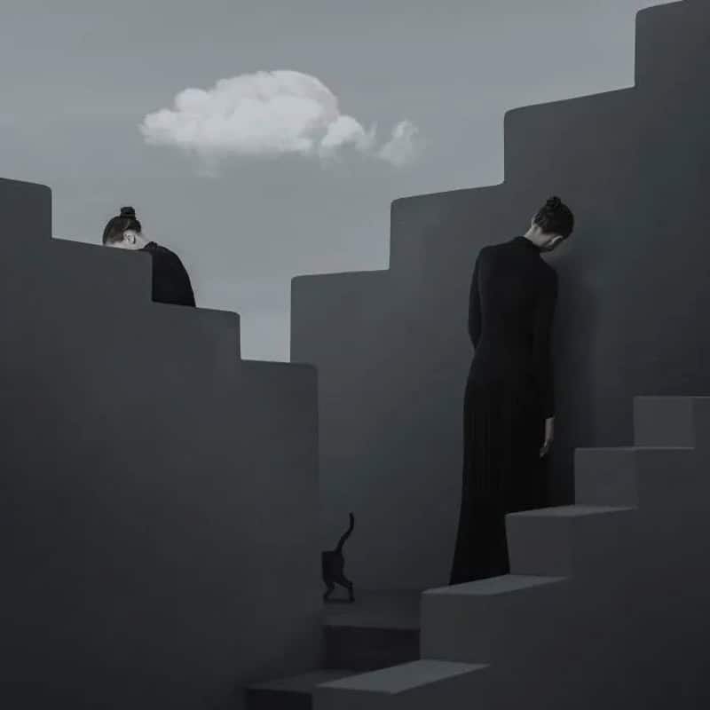 Two women in black dresses with their heads bowed, surrounded by gray stairs and a small black cat.