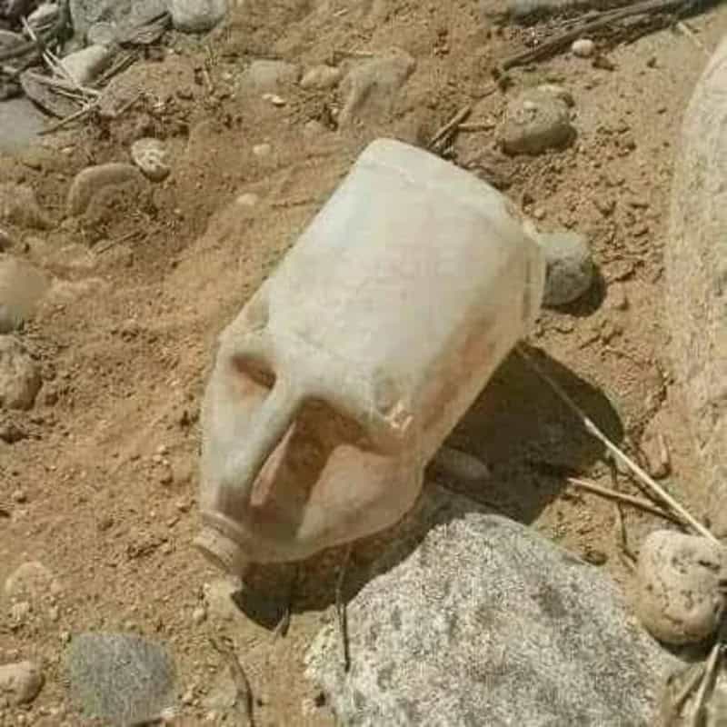 Object resembling a skull with a bottle neck, lying on dirt with rocks.