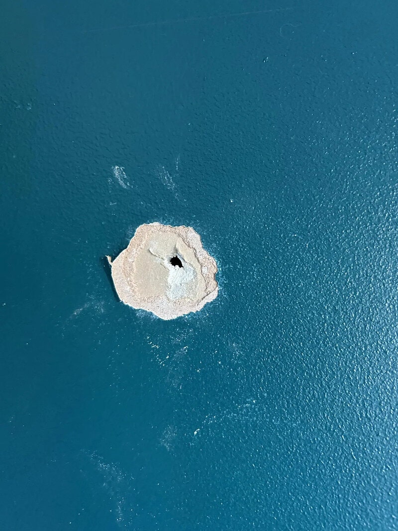 Hole in blue wall with chipped paint around it.