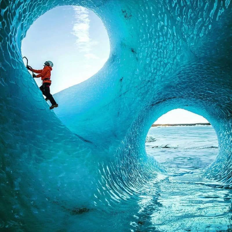 Climber in red gear ascending inside a blue ice cave with circular openings.