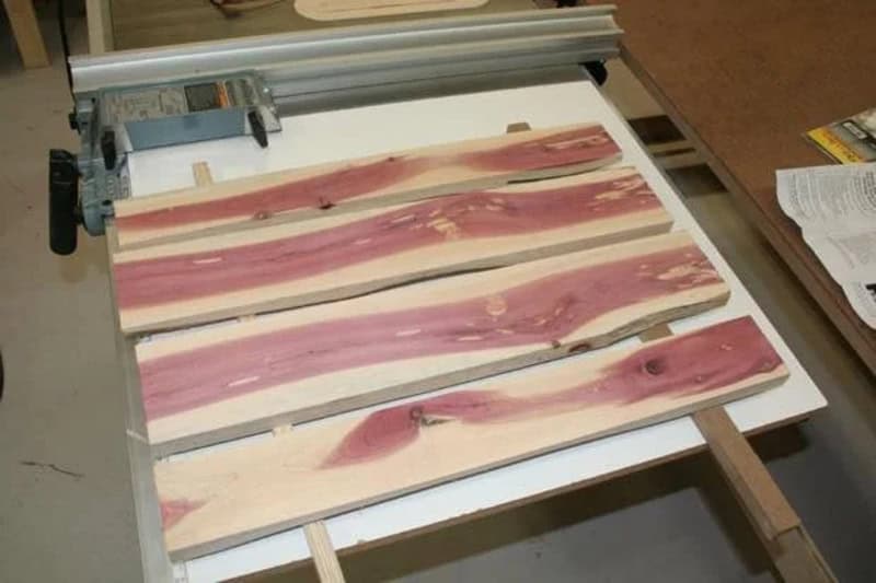 Wooden planks with pink and beige streaks on a saw table.
