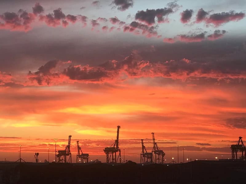 Sunset over oil rigs with colorful sky and clouds.