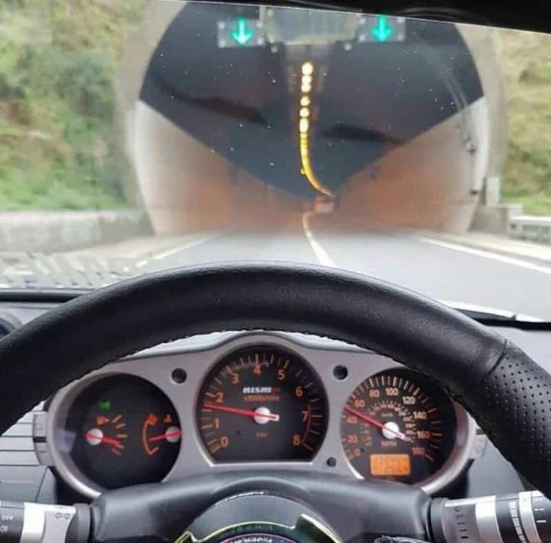 View from inside a car approaching a tunnel with green arrow signs above.
