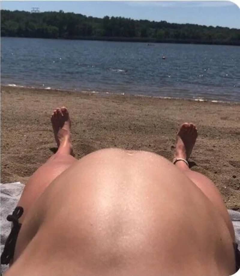 Person lying on a beach with a view of the water and trees in the background.