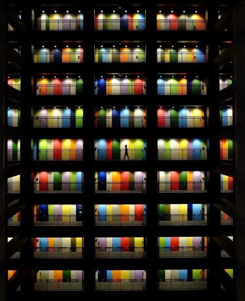 Colorful books on shelves in a multi-story library with a person walking.