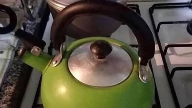 Green kettle with a black handle on a stove.