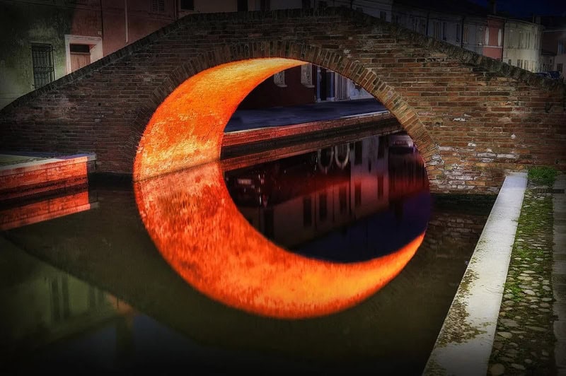 Bridge over water with a glowing orange crescent reflection.