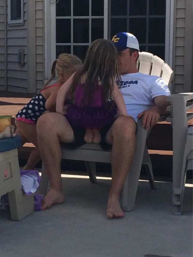 Man with two young girls sitting on his lap outside on a deck.