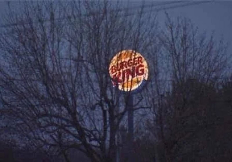 Burger King sign visible through leafless trees at night.
