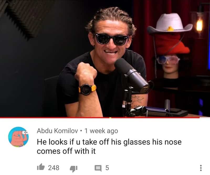 Man with sunglasses smiling, sitting in a recording studio with a microphone.