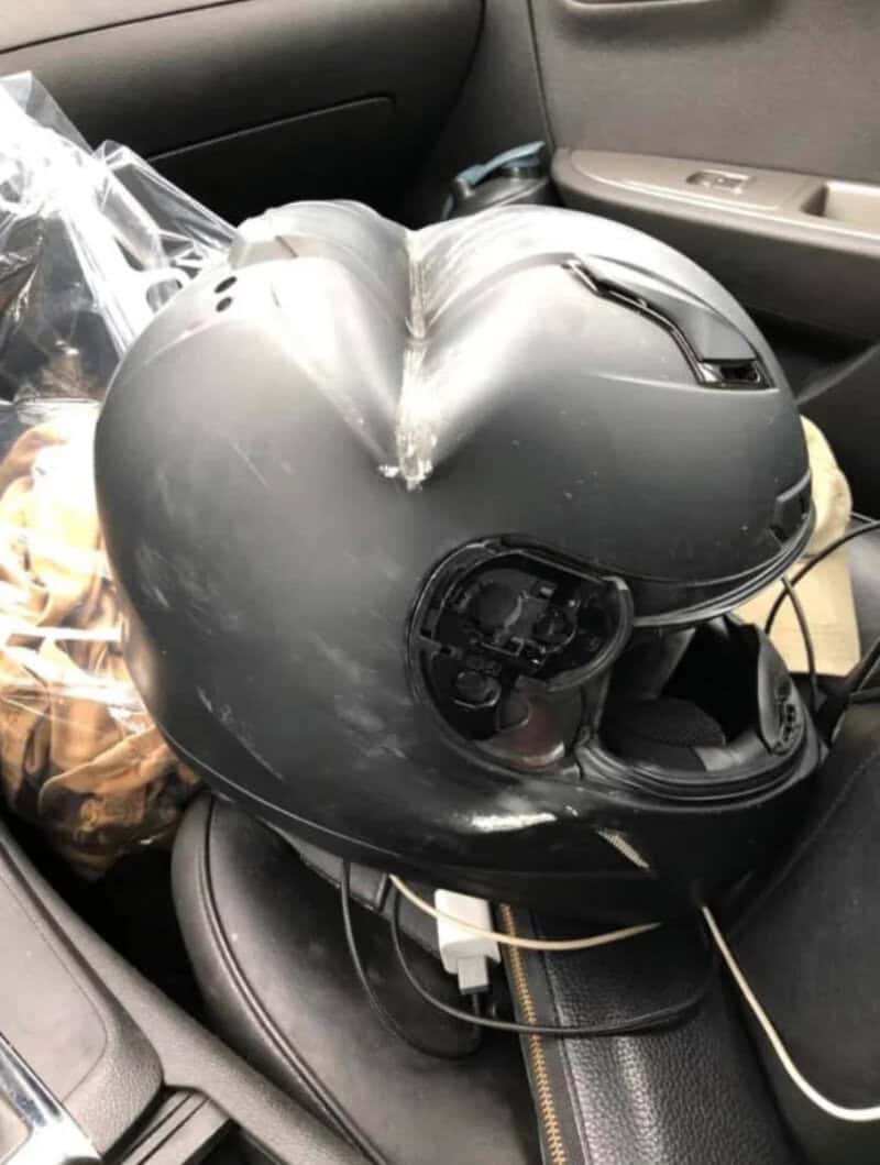 Black motorcycle helmet with open visor on car seat, connected to charger.