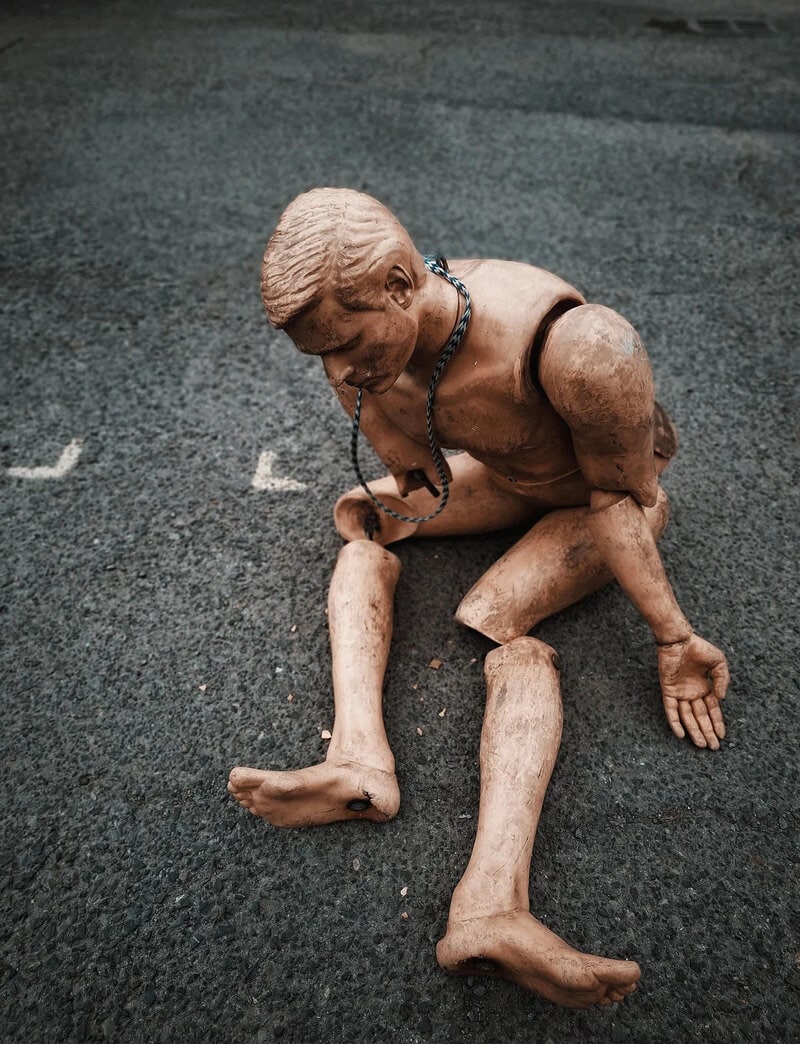 Broken doll of a boy with a chain around his neck on the ground.