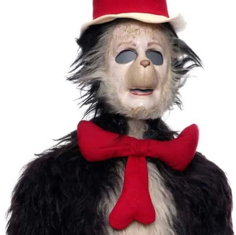A creepy monkey costume with a white face, black eyes, red hat, and red bow tie.