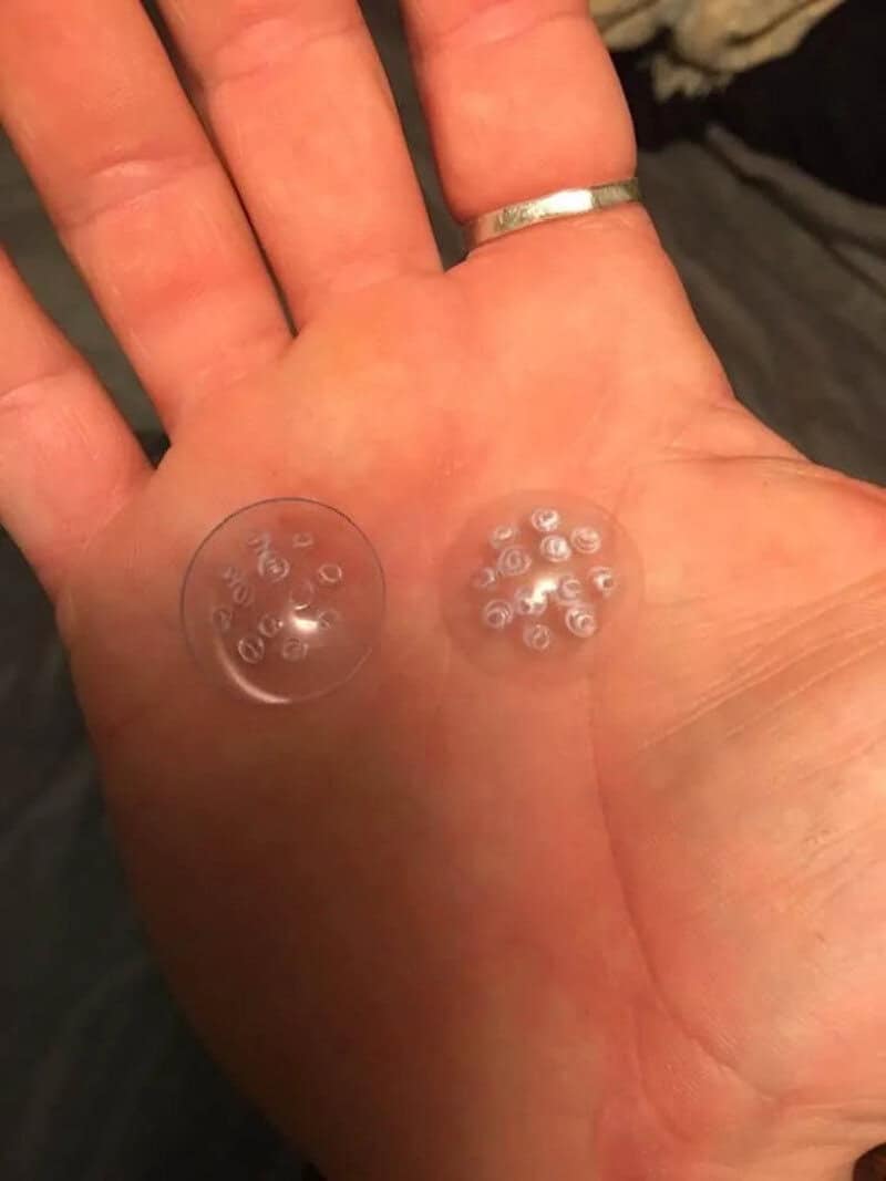 Hand with two small transparent capsules, one with tiny objects inside, on a hand.